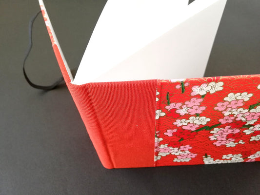 Petit carnet artisanal en reliure classique, couverture en papier washi rouge à motifs floraux blancs et rouges, bandeau.