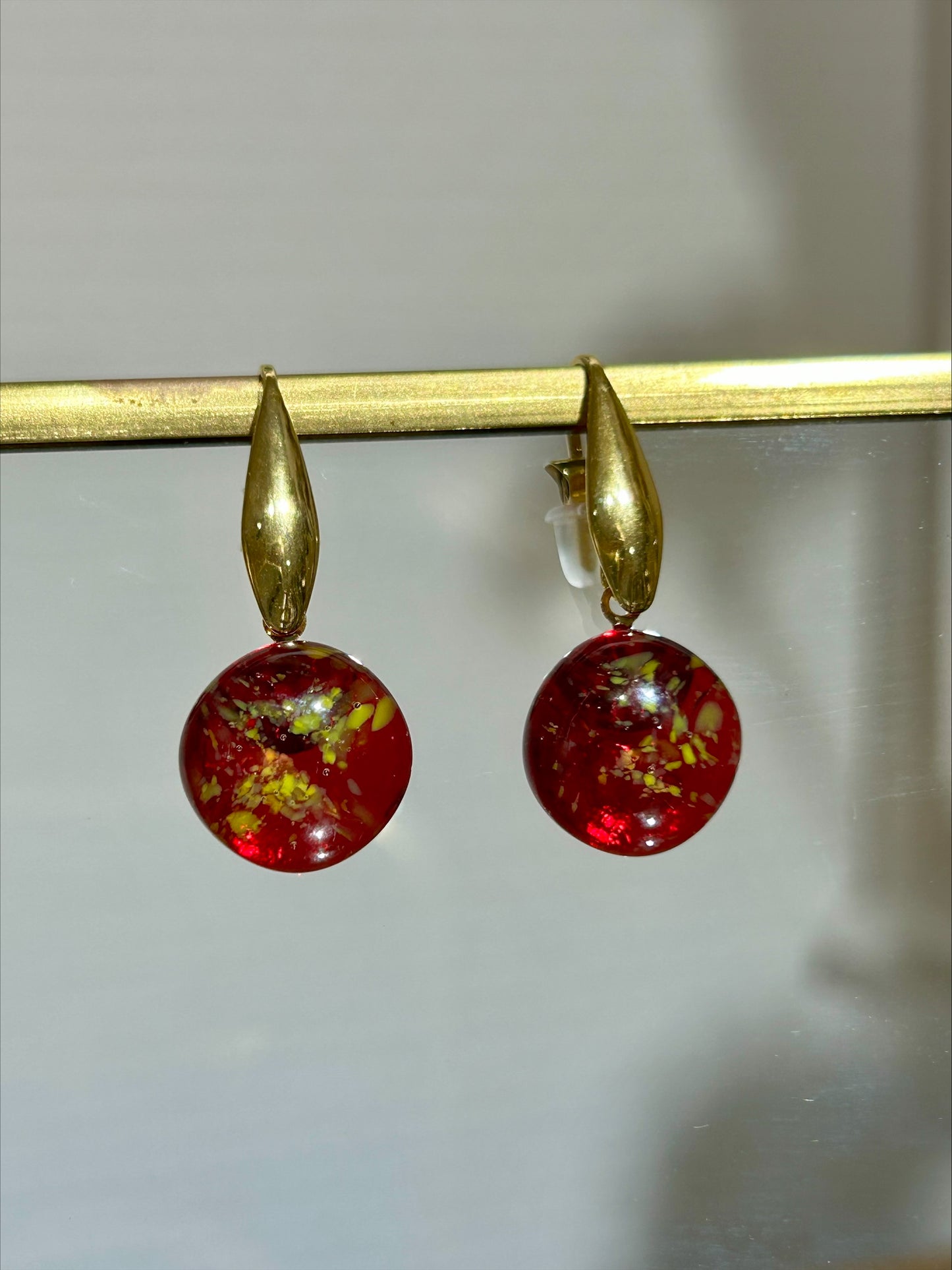Boucles d'oreilles artisanales en laiton doré avec pendentifs ronds rouges marbrés, bijou fait main éco-responsable.