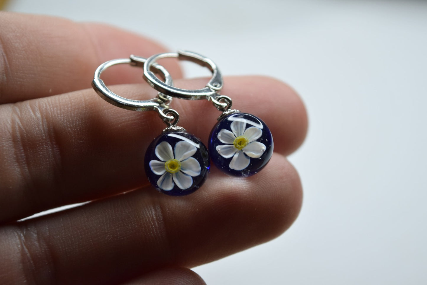 Créole artisanale en verre bleu avec fleur de narcisse blanche délicate, bijou fait main éco-responsable.