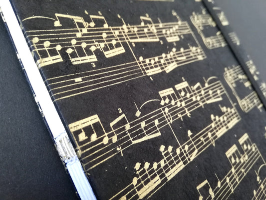 Carnet A5 artisanal à couverture en papier noir orné de partitions musicales blanches, création artisanale unique et produit .