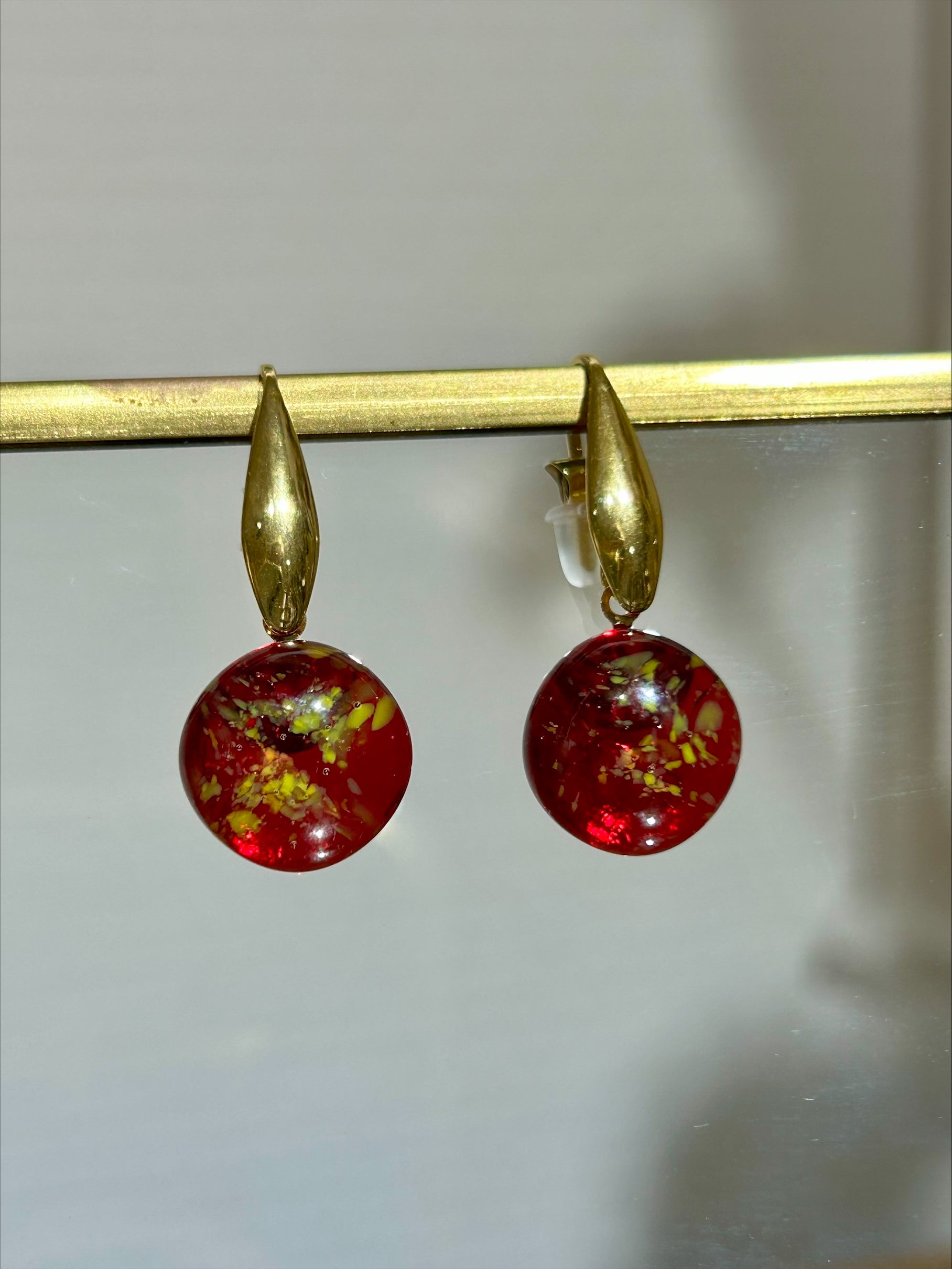 Boucles d'oreilles artisanales en laiton doré avec pendentifs ronds rouges marbrés, bijou fait main éco-responsable.